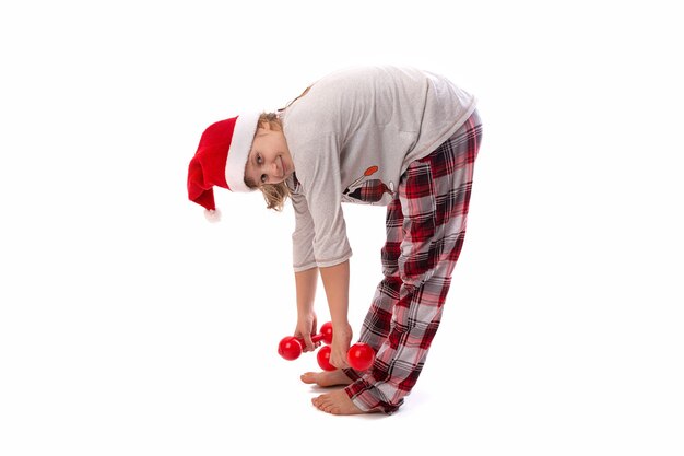 Ładny zabawny asystent Świętego Mikołaja robi fitness z czerwonymi hantlami na białym tle. Pojęcie świąt Bożego Narodzenia. Obchody Nowego Roku.