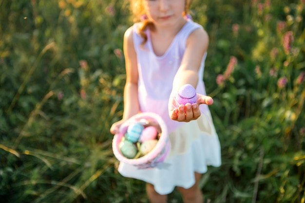 Ładny zabawny dziewczyna z pisanki na wiosnę w przyrodzie w polu ze złotym światłem słonecznym i kwiatami. Święta Wielkanocne, Zajączek z uszami, kolorowe jajka w koszu. Styl życia