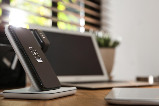 Ładowanie telefonu komórkowego i smartwatcha za pomocą bezprzewodowej podkładki na drewnianym biurku na tekst Nowoczesne urządzenie do pracy