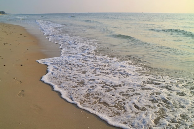 Łagodne fale biją na plaży ze śladami piasku i błękitnym niebem z odbiciem w letni poranek