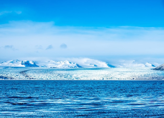 Laguna lodowcowa Jokulsarlon z lodowcem i dużą górą lodową pod zachmurzonym błękitnym niebem na Islandii