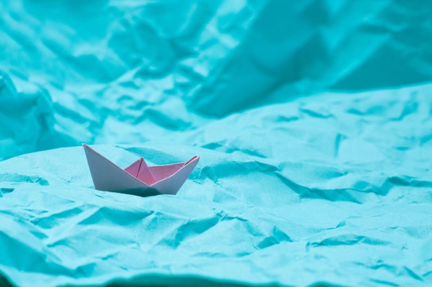 Lakoniczne zdjęcie zgniecionego niebieskiego papieru imitującego morze, a na nim małą różową łódkę origami