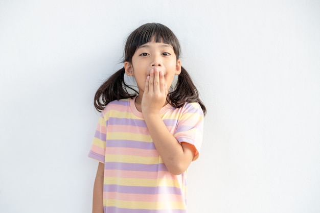 Łał. Ujęcie w studio przedstawiające emocjonalną, uroczą dziewczynkę Azjatkę unoszącą brwi i zakrywającą otwarte usta dłonią, która jest zaskoczona i zszokowana, pokazując naprawdę zdumioną reakcję na nieoczekiwane wiadomości
