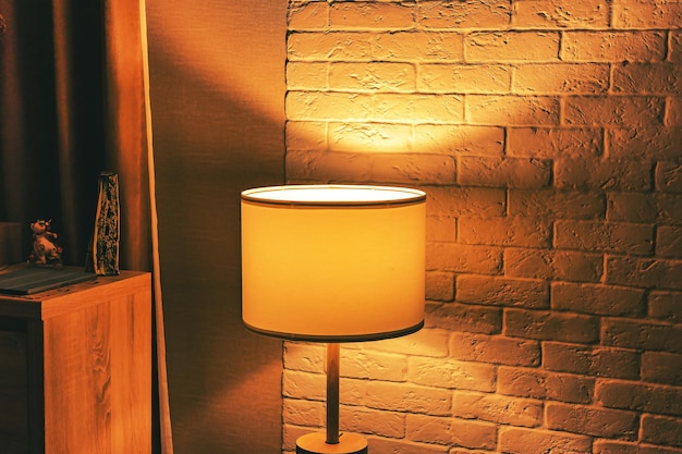 Lampa podłogowa retro z delikatnym żółtym światłem we wnętrzu mieszkania na tle teksturowanej białej ściany z cegły