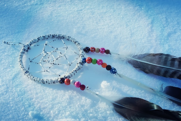 Zdjęcie Łapacz snów na tle śniegu. ręcznie wykonany wystrój z piórami i kolorowymi koralikami.