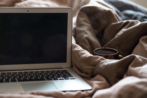 laptop i filiżanka kawy lub herbaty na łóżku z szarymi prześcieradłami praca w domu przytulna praca