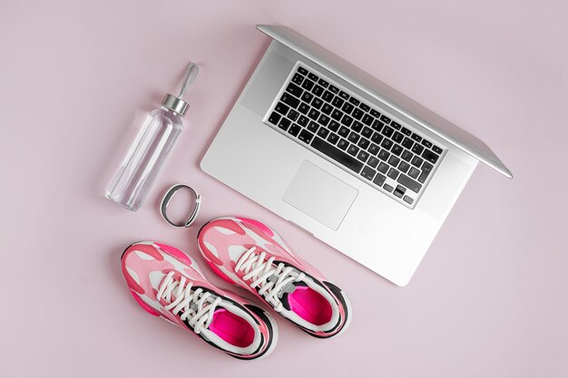 Laptop, trampki i bidon na różowym tle. Program fitness online. Trening w domu.