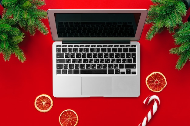Laptop z futerkowymi gałąź i boże narodzenie dekoracjami na czerwonego tła odgórnym widoku