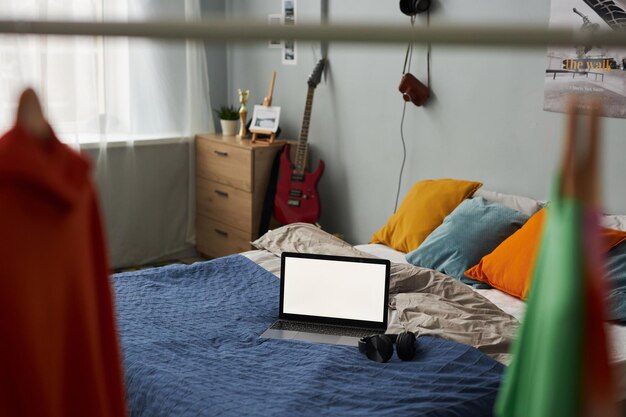 Laptop z pustym ekranem stojący na podwójnym łóżku z poduszkami