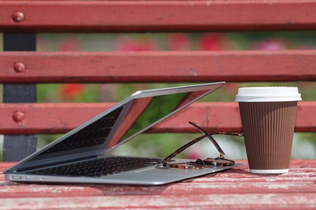 Laptop z szkłami i notatnika lying on the beach na ławce w miasto parku, Plenerowej nauce lub Internetowym Freelance Pracującym pojęciu