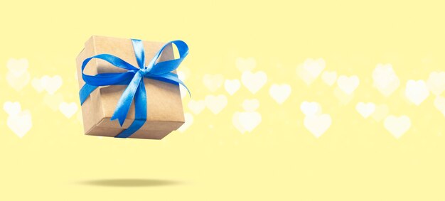 Latające pudełko na jasnożółtej powierzchni z bokeh w kształcie serca. Koncepcja wakacje, prezent, sprzedaż, ślub i urodziny. .