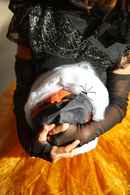 Latarnia z dyni, dynia halloween w ochronie medycznej Czarna maska w rękach dziewczyny podczas uroczystości Halloween w domu Covid19 Pandemia koronawirusa, kopia przestrzeń