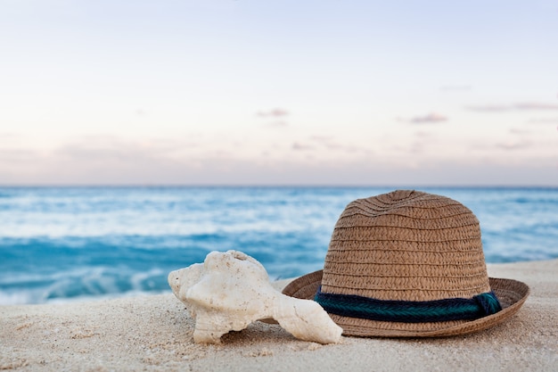 Lato słomkowy kapelusz i muszli na piaszczystej plaży o wschodzie słońca