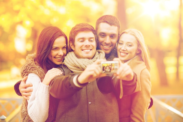 lato, wakacje, wakacje, podróże, turystyka, koncepcja szczęśliwych ludzi - grupa przyjaciół lub par bawiących się aparatem fotograficznym w jesiennym parku