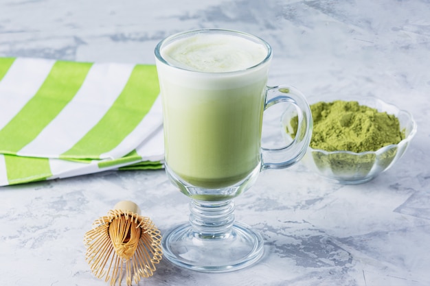 Latte z zielonej herbaty Matcha z proszkiem matcha i trzepaczką bambusową. Zdrowy napój w przezroczystym szklanym zbliżeniu