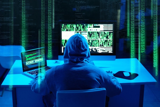 Łatwe przechodzenie przez zaporę sieciową Ujęcie z tyłu przedstawiające hakera, który łamie kod komputera w ciemności