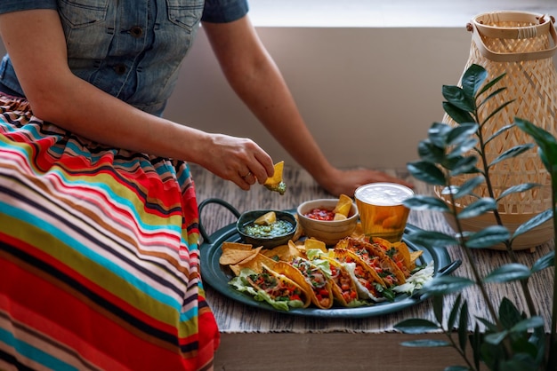 Zdjęcie latynoamerykańska kobieta w tradycyjnej kolorowej spódnicy jedząca kurczaka tacos nachos salsa i guacamole