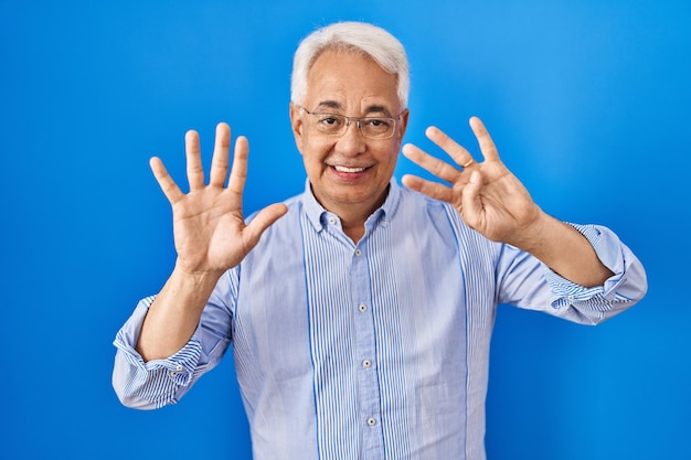 Latynos starszy mężczyzna w okularach pokazujący i wskazujący palcami numer dziewięć, uśmiechając się pewnie i szczęśliwie