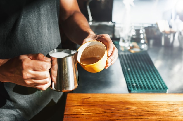 Latynos trzymający żółtą filiżankę i stalową karafkę przygotowujący latte w kawiarni