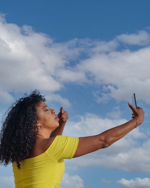 Latynoska czarna kobieta sprawia, że autoportret z mobilnych na zewnątrz, błękitne niebo.