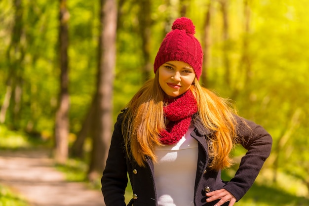 Latynoska dziewczyna w czarnej kurtce, szaliku i czerwonej wełnianej czapce, ciesząca się jesiennym parkiem, z odrobiną chłodu w parku