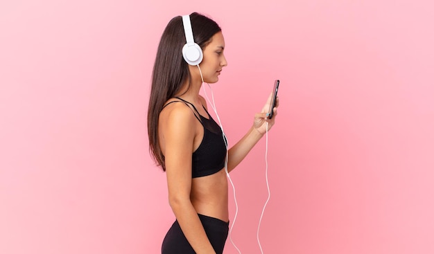 Latynoska kobieta fitness na widoku profilu myśląca, wyobrażająca sobie lub marząca na jawie ze słuchawkami i telefonem