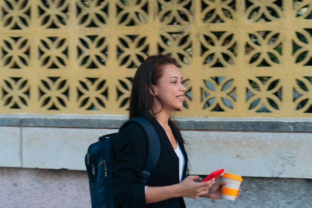 Latynoska kobieta idzie do pracy rano. Kobieta szła do pracy trzymając telefon komórkowy i gorącą kawę.