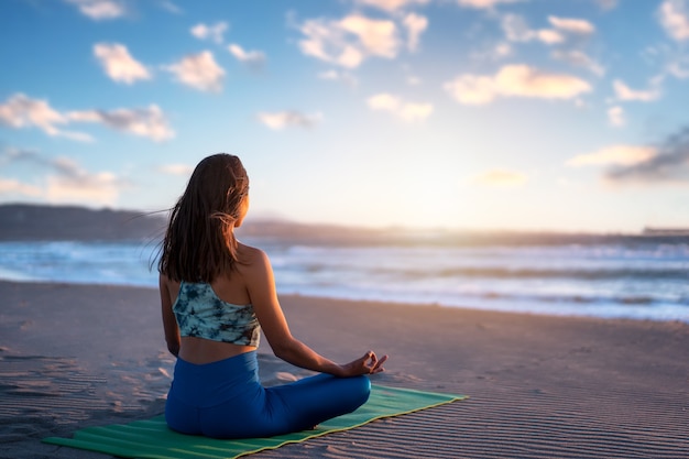 Latynoska kobieta medytuje lub robi jogę o zachodzie słońca na plaży