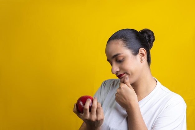 Latynoska kobieta myśli o zjedzeniu czerwonego jabłka na żółtym tle