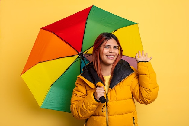 Latynoska kobieta uśmiecha się radośnie machając ręką witając cię i witając cię koncepcja deszczu i parasola