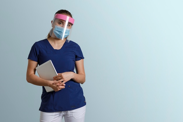 Latynoska kobieta w mundurze pielęgniarki, nosząca maskę i osłonę twarzy, trzymająca cyfrowy tablet