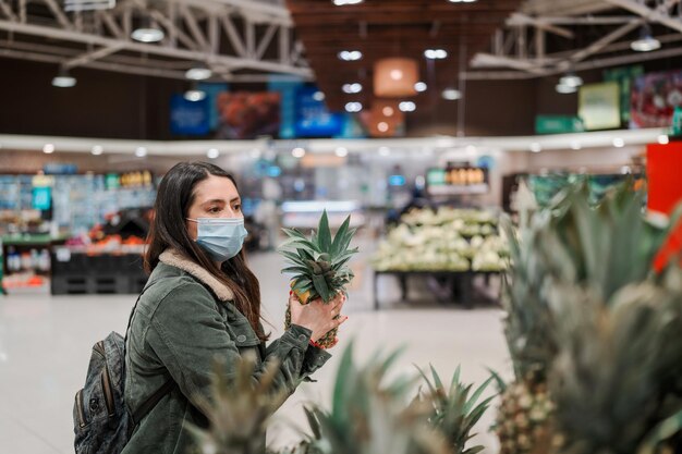 Latynoska kobieta z maską na twarz w supermarkecie kupuje artykuły spożywcze lub owoce