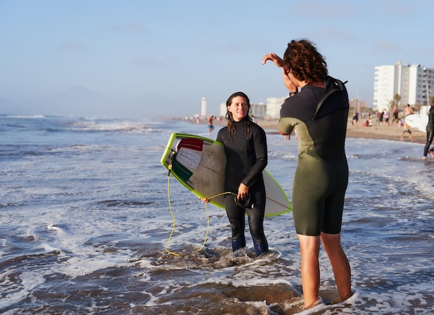 Latynoska surferka słucha swojego instruktora surfingu udzielającego instrukcji na brzegu plaży