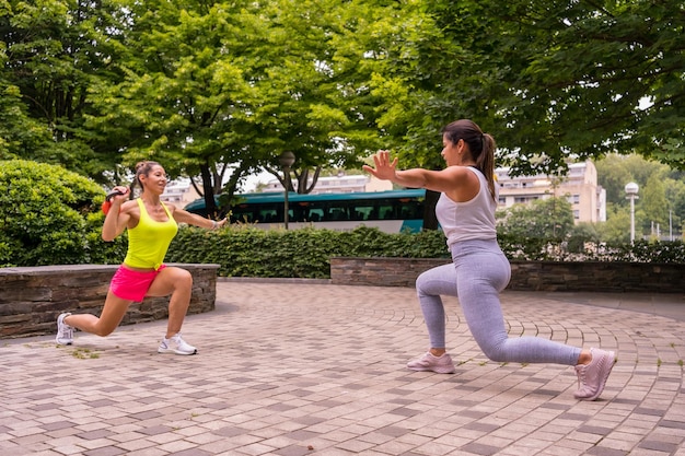 Latynoska uprawiająca sport w parku w mieście, zdrowy tryb życia, dwie dziewczyny ćwiczące rozciąganie ciężarów i przysiady