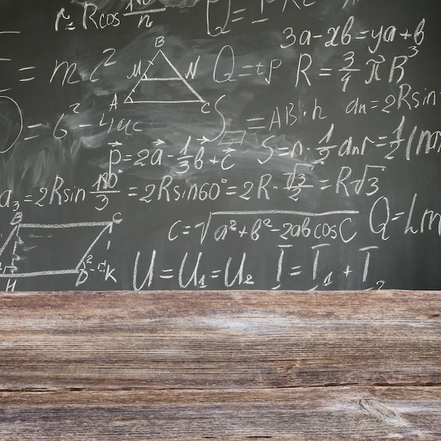 Zdjęcie Ławka szkolna z formuł matematycznych napisanych białą kredą na tle czarnej tablicy