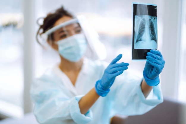 Lekarka w daszku i rękawiczkach ochronnych bada zdjęcie rentgenowskie pacjenta