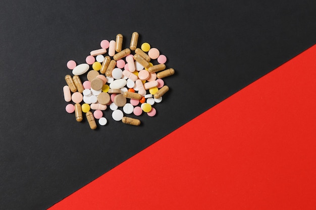 Lekarstwa białe kolorowe okrągłe tabletki ułożone streszczenie na czerwonym tle czarnym. Aspiryna, kapsułki do projektowania. Zdrowie, leczenie, wybór koncepcji zdrowego stylu życia. Skopiuj miejsce na reklamę.