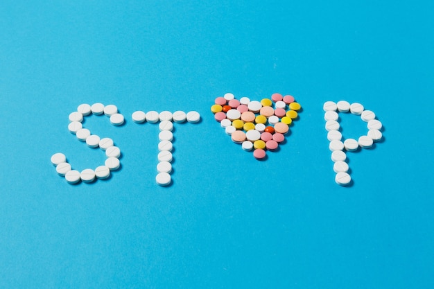 Lekarstwa białe, kolorowe okrągłe tabletki w słowie Stop na białym tle na niebieskim tle