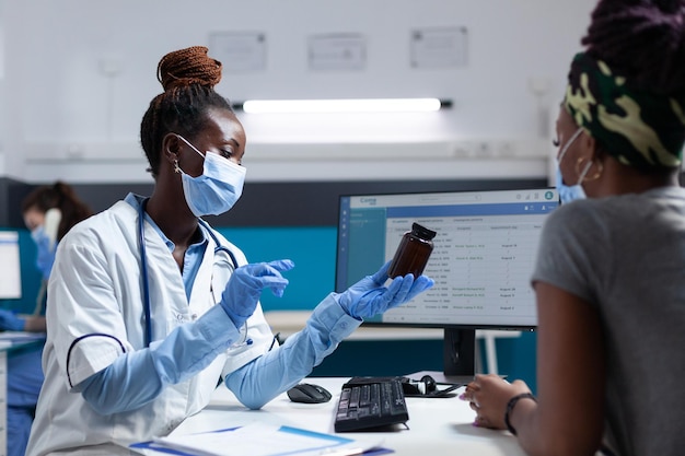 Lekarz afroamerykanin lekarz trzymający butelkę pigułek omawiający leczenie chorego pacjenta podczas wizyty klinicznej w gabinecie szpitalnym. Lekarz medyk wyjaśniający objawy choroby