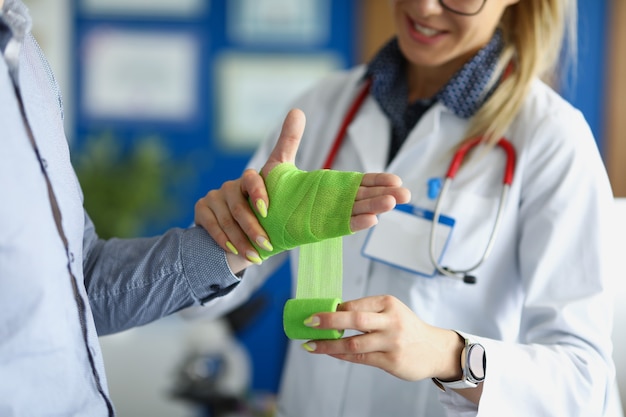 Lekarz bandażujący ranę na ramieniu pacjenta z zielonym bandażem w zbliżenie kliniki