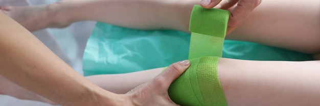 Lekarz bandażuje bolącą nogę dziecka zielonym bandażem w zbliżeniu kliniki