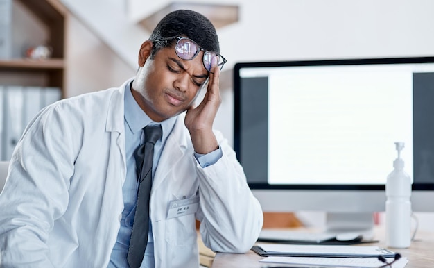 Lekarz cierpiący na stres i ból głowy podczas pracy w szpitalu Młody zmęczony pracownik służby zdrowia odczuwa presję dużego obciążenia pracą podczas pandemii koronawirusa