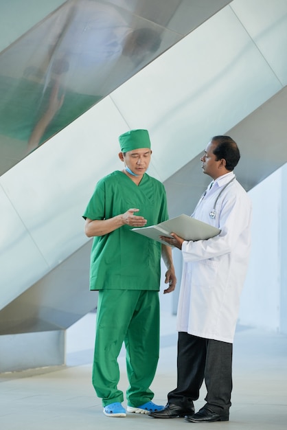 Lekarz i chirurg stojący w sali szpitalnej i omawiający historię medyczną pacjenta