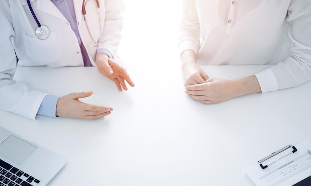 Lekarz i pacjent omawiają aktualne kwestie zdrowotne, siedząc blisko siebie przy stole w klinice, po prostu zbliżenie rąk. Koncepcja medycyny.