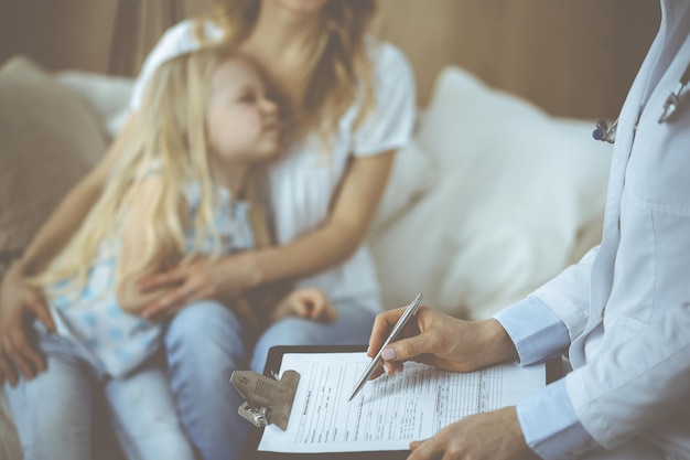 Lekarz i pacjent. Pediatra za pomocą schowka podczas badania małej dziewczynki z matką w domu. Chore i nieszczęśliwe dziecko na egzaminie lekarskim. Koncepcja medycyny.