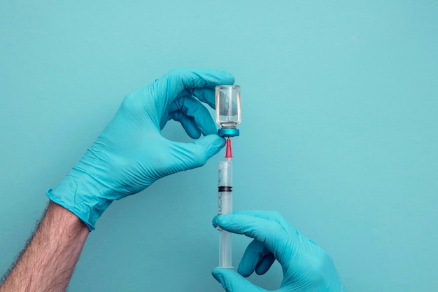 Lekarz lub pielęgniarka w niebieskich rękawiczkach chirurgicznych trzymająca strzykawkę i dawkę szczepionki