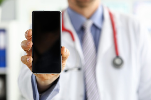Lekarz medycyny mężczyzna posiadający telefon komórkowy i pokazując go w biurze. Sprzęt medyczny nowoczesna technologia i koncepcja komunikacji. Terapeuta korzystający z wyszukiwania informacji na smartfonie