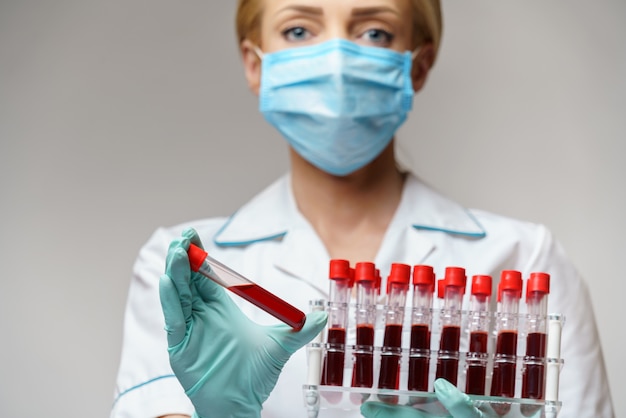 Zdjęcie lekarz medycyny pielęgniarki kobieta jest ubranym maskę ochronną i rękawiczki - trzyma stojaka z wirusowymi badaniami krwi