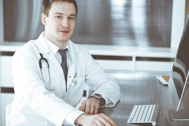 Lekarz mężczyzna siedzi za komputerem w miejscu pracy w klinice lub biurze szpitala Medic headshot i medycyna koncepcja