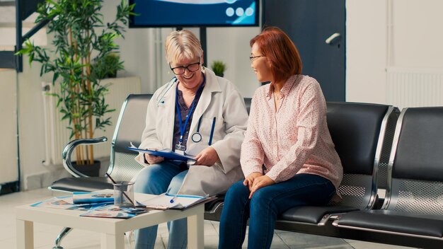 Lekarz ogólny uczestniczący w wizycie kontrolnej z pacjentem azjatyckim w holu poczekalni, rozmawiający o diagnozie medycznej i leczeniu. Starszy lekarz i kobieta robi egzamin konsultacyjny.
